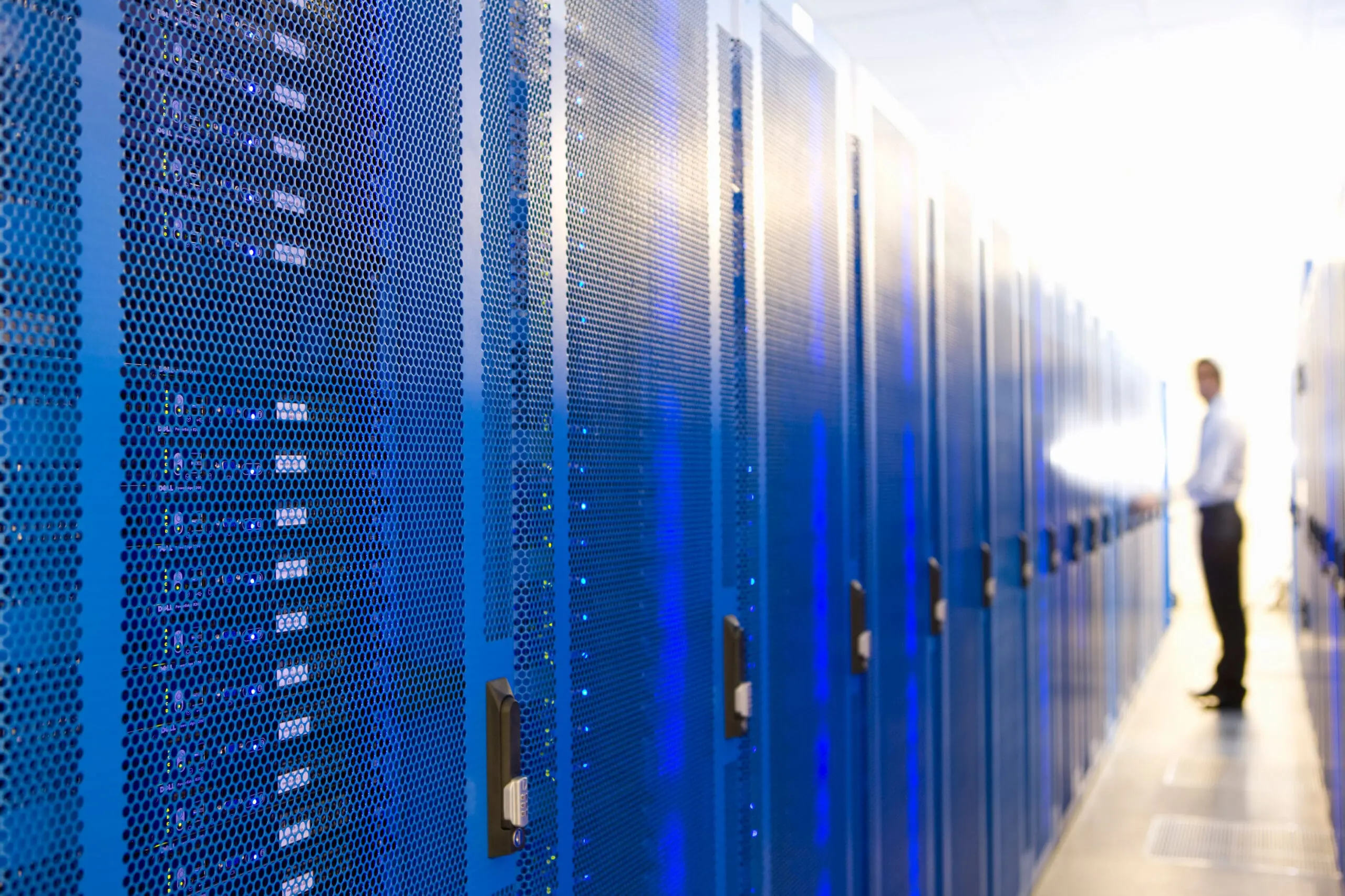 Fila de gabinetes de servidores de red iluminados en azul brillante dentro de un centro de datos corporativo. Ilustra las opciones de infraestructura tecnológica, desde arquitecturas monolíticas hasta microservicios, y la gestión eficiente en la nube mediante partners institucionales como AWS.