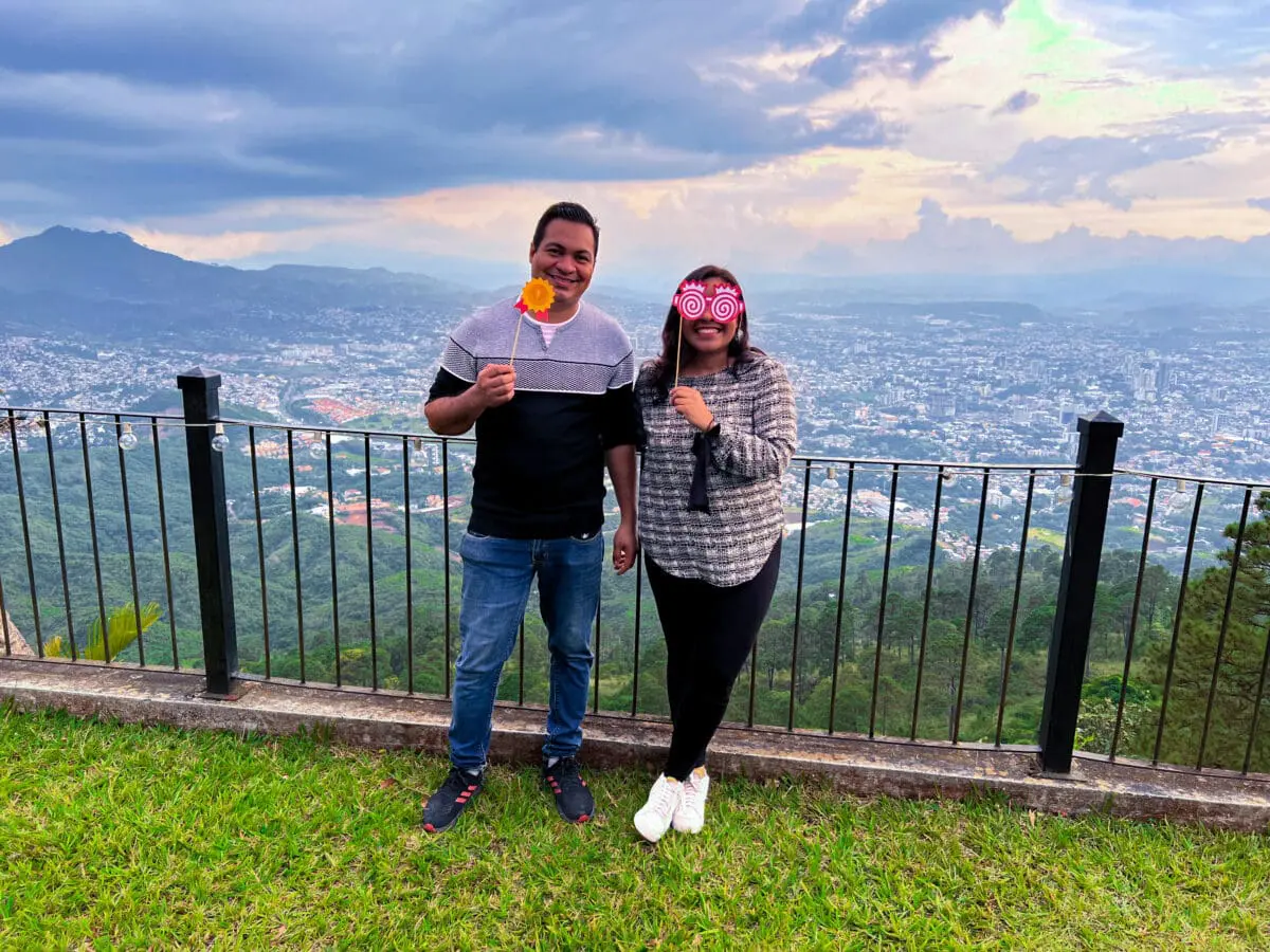 Dos colaboradores de Andes Development sonriendo y utilizando accesorios festivos durante la convivencia corporativa del 12º aniversario. Al fondo se observa una impresionante vista panorámica de la ciudad y las montañas al atardecer.