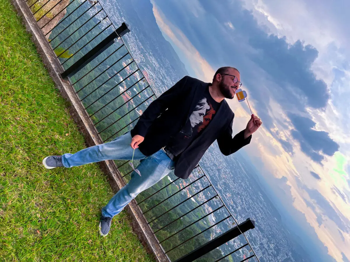 Colaborador del equipo de Andes Development posando de forma divertida con un accesorio fotográfico durante la celebración del 12º aniversario de la agencia, con una vista panorámica de la ciudad al fondo. Refleja la cultura laboral positiva y dinámica de la empresa.