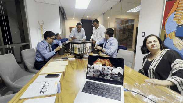 Animación de una sesión de consultoría estratégica corporativa facilitada por Andes Development para la empresa Proteger. Un grupo de ejecutivos participa alegremente en una dinámica de trabajo en equipo en una sala de juntas, mientras una laptop en primer plano muestra la presentación visual con la analogía de una 'mina de oro' para ilustrar el potencial de la empresa.