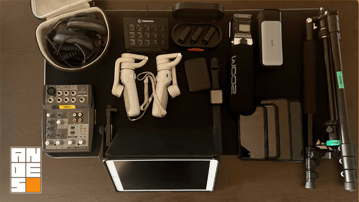 Kit completo de equipo móvil utilizado en Andes para la producción de videos de marketing. La vista superior (flatlay) detalla estabilizadores DJI, micrófonos Rode y Zoom, mezcladora de audio Behringer, Stream Deck, batería externa Anker, trípodes y múltiples dispositivos iPhone Pro. Representa el hardware esencial recomendado para producciones cinematográficas móviles.