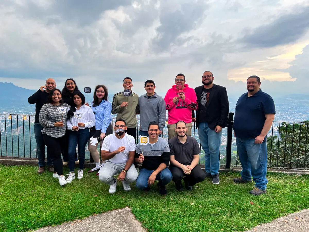 Fotografía grupal de los colaboradores de Andes Development posando con creativos accesorios de cabina de fotos (photo booth) en un mirador. Representa la celebración del 12º aniversario y el excelente ambiente laboral de la empresa con la ciudad de fondo.