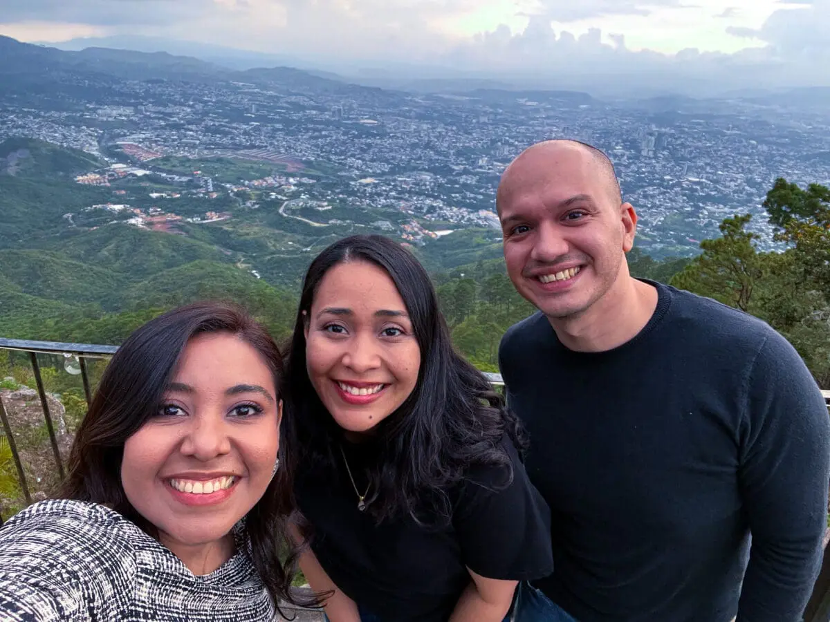 Selfie de tres integrantes del equipo de Andes Development disfrutando de la convivencia corporativa por el 12º aniversario. Los colaboradores posan sonrientes al aire libre con un hermoso paisaje urbano y natural a sus espaldas.