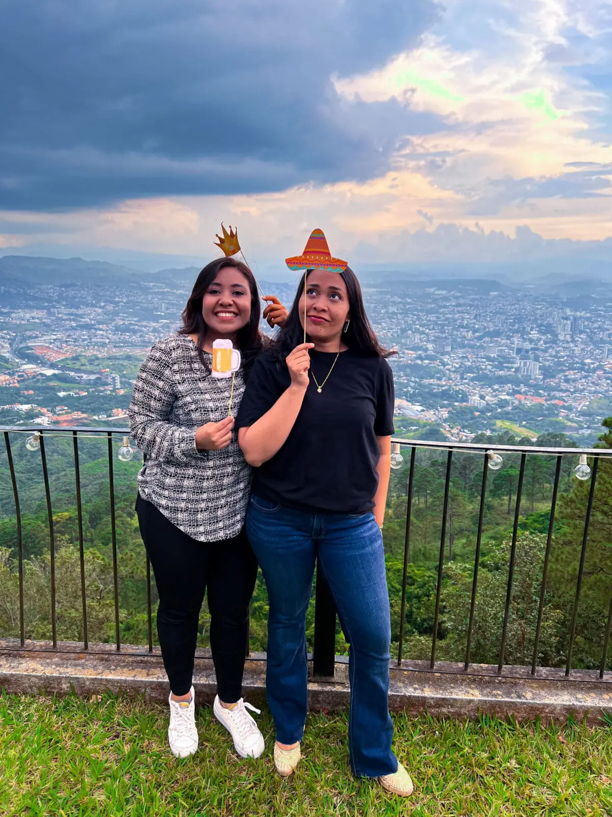 Dos colaboradoras del equipo de Andes Development posando alegremente con accesorios fotográficos festivos (sombrero y cerveza) en la convivencia del 12º aniversario de la agencia, demostrando la positiva cultura de la empresa.